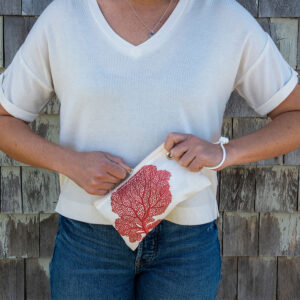 Person holding a small white bag featuring a red coral design