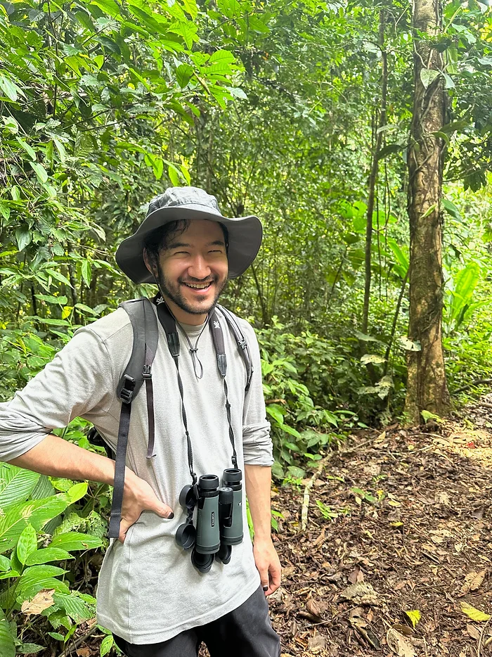 Indigo Dandelion Lee Mané posing with safari hat on and camera hanging around their neck on a nature trail