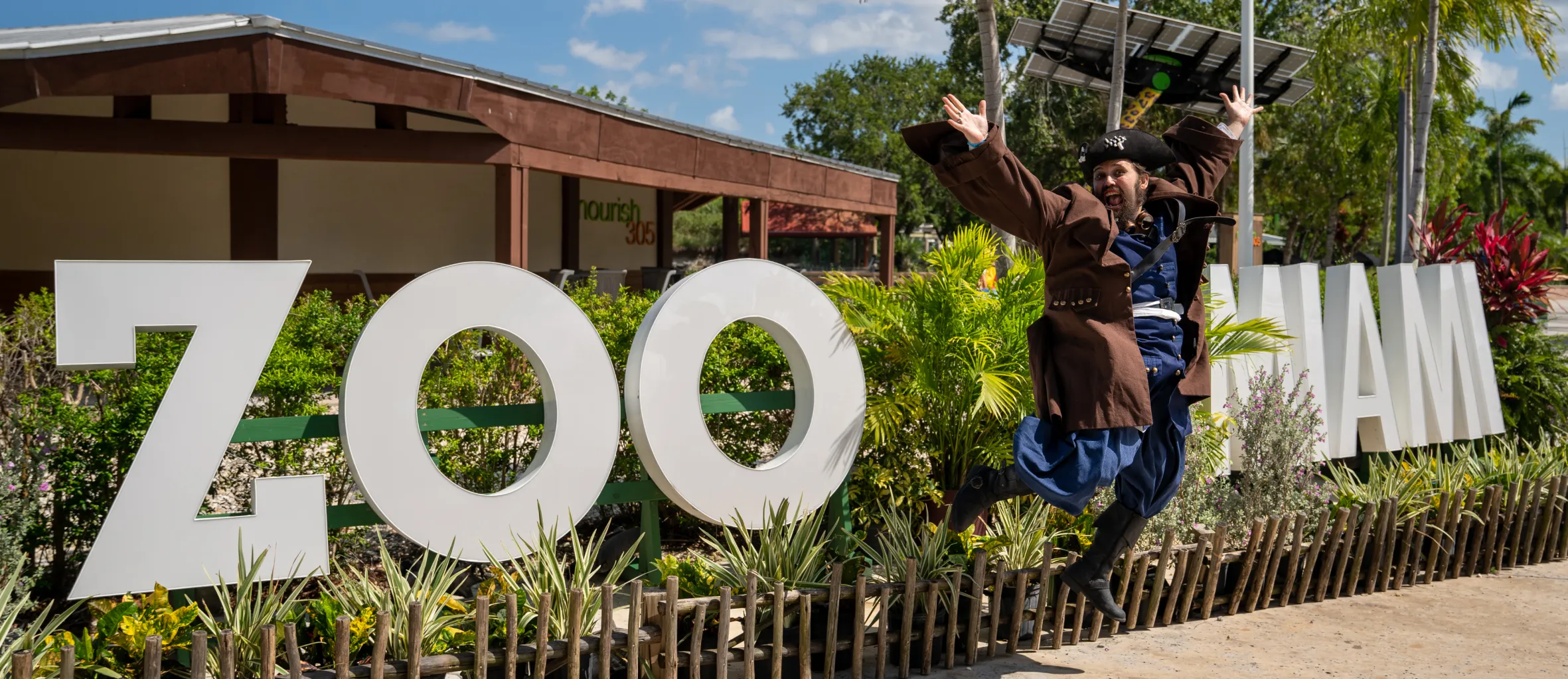 Captain Coral dressed as a pirate jumping in front of the Miami Zoo sign