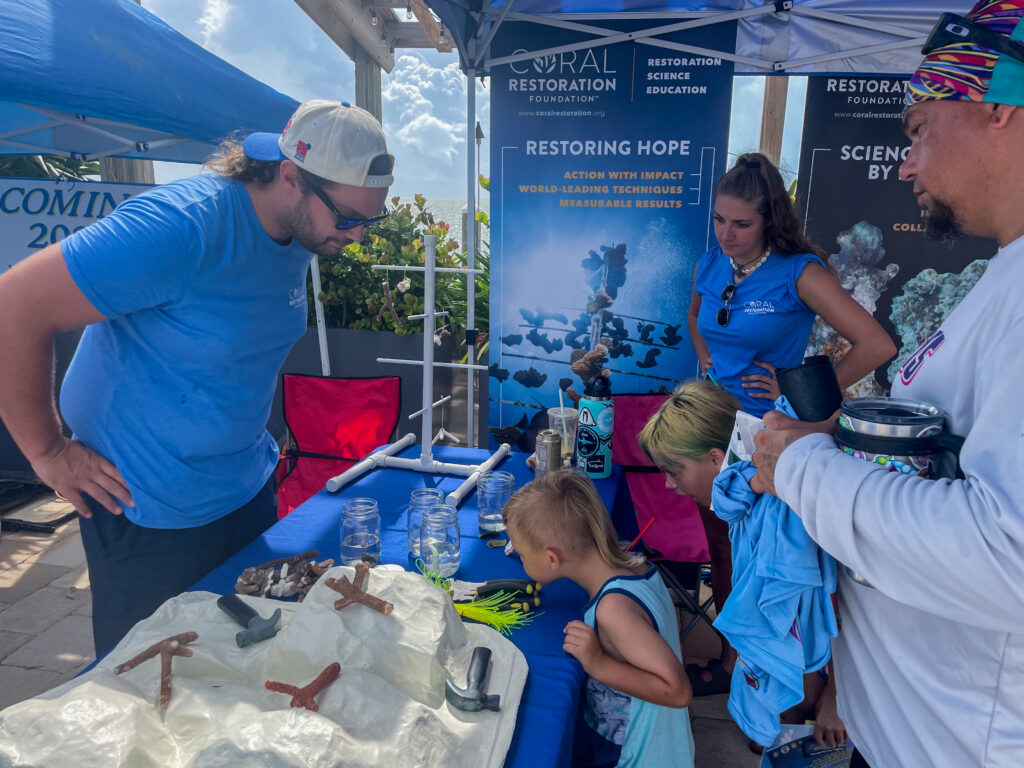 A Coral Restoration Foundation educator interacts with children and families at a community outreach booth, teaching about coral reef restoration.