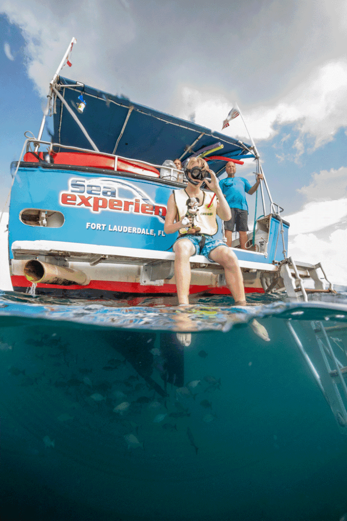 A child wearing a snorkel mask sits on the edge of the Sea Experience boat in Fort Lauderdale, preparing to enter the water.