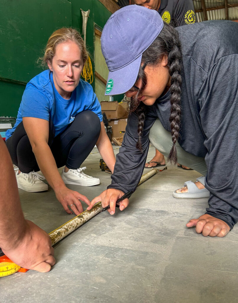 Two participants, including Nikkie Cox, measure a PVC pipe while preparing materials for Coral Tree™ construction.