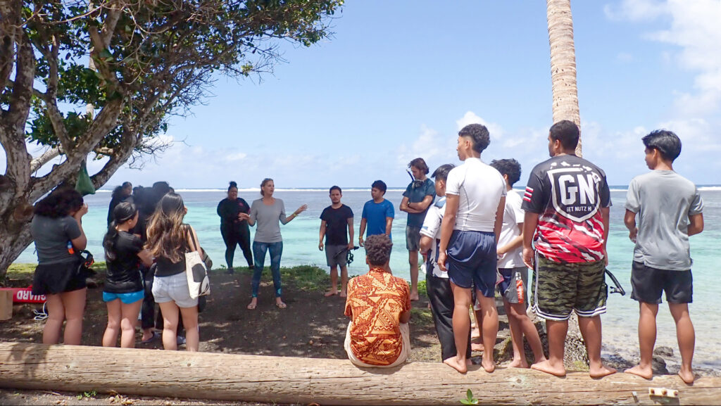 A group of students and teachers gather near the shore as a CRF™ staff member explains coral reef ecology.