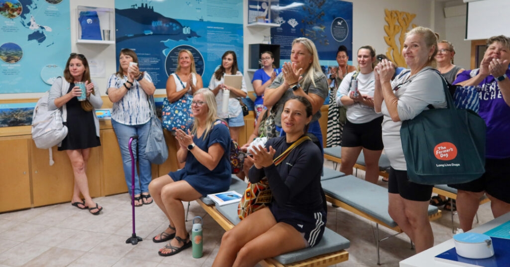 A group of educators gathers inside the CRF™ Exploration Center in Key Largo, clapping and smiling during an ocean science presentation.