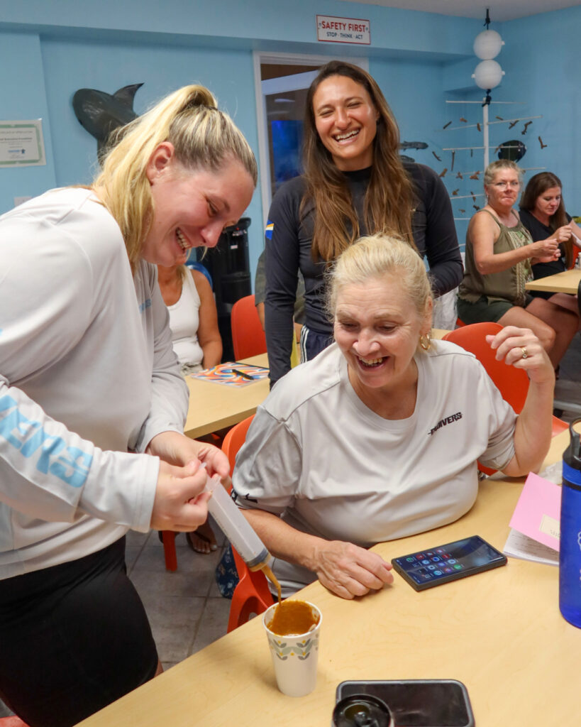 Three educators laugh while conducting CRF’s Maritime Slime Workshop, testing different “marine slime” formulas to explore how mucus protects coral and fish.