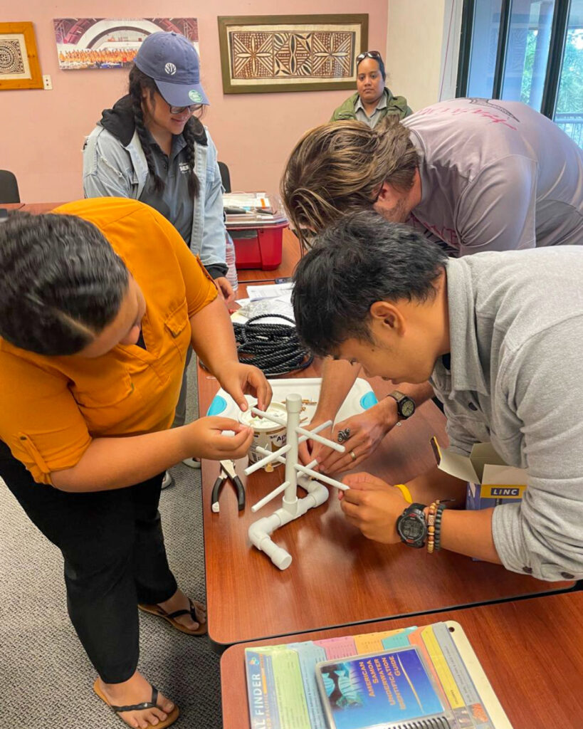 A group of participants works together around a table to assemble a small Coral Tree™ model.