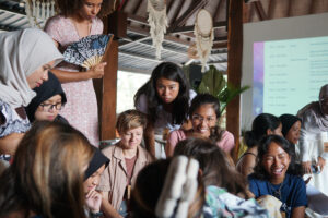A diverse group of women gathers in an open-air venue at the Coral Catch Conference, smiling and collaborating during a workshop session focused on coral restoration and community building.
