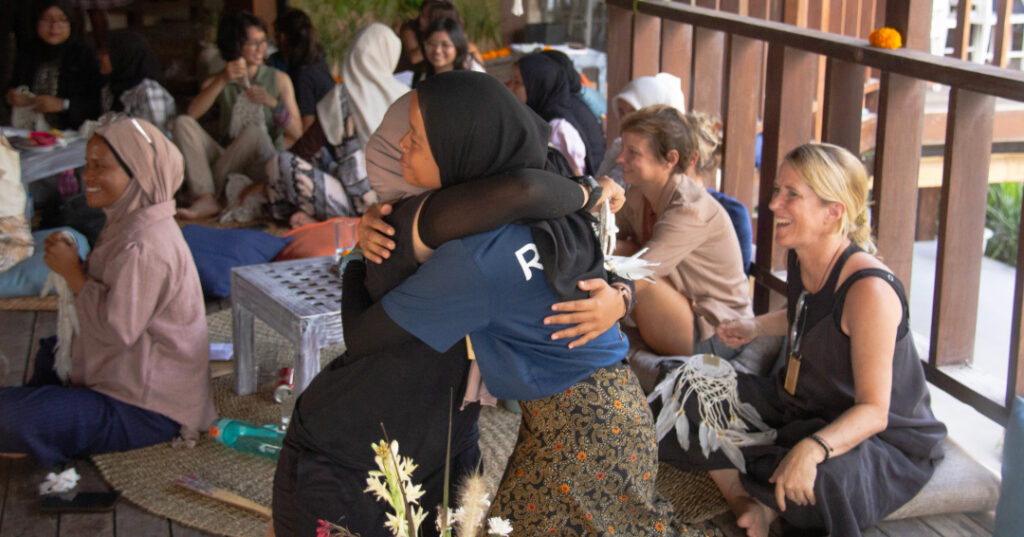 Two women embrace at the Coral Catch Conference surrounded by other participants, capturing a moment of connection and solidarity among conservationists dedicated to reef restoration.