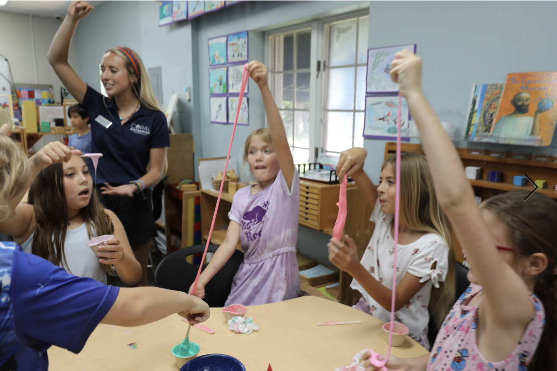 A Coral Restoration Foundation educator leads a hands-on classroom activity where several young students excitedly stretch colorful slime at a table. Artwork hangs on the walls behind them, capturing an interactive marine science learning experience.